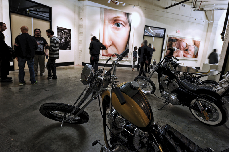 A view of the exhibit with Morgan’s motorcycles. In the background are Coatney’s paintings and one of Jordan Conway’s photographs, this one featuring Morgan in his shop, to the left of the frame.